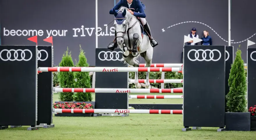 Un cavalier et son cheval gris s'envolent au-dessus d'une haie, défiant le fahrenheit de vains. Les logos Audi et le slogan "become your rivals" ornent le fond.