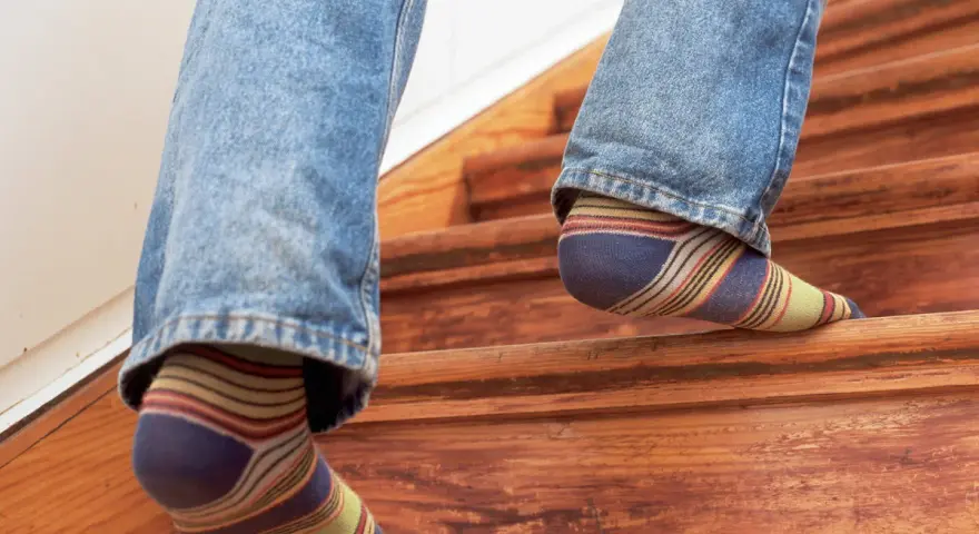 Füße in bunten Socken steigen eine Holztreppe hinauf, die auf eine Renovierung wartet.