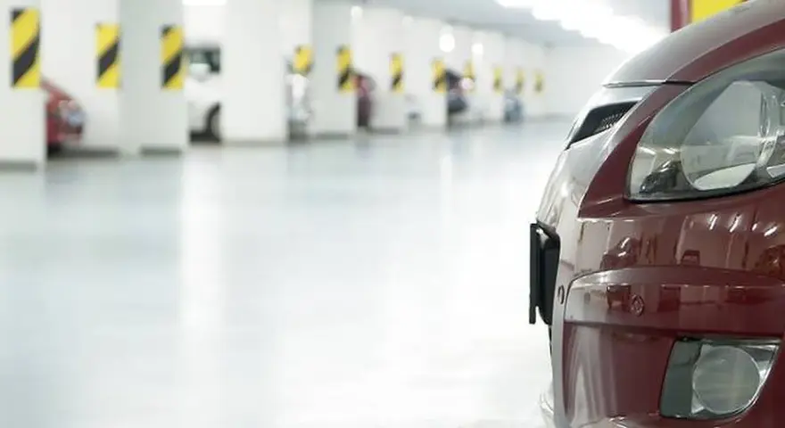 Czerwony samochód na tle rzędu miejsc parkingowych. Zastanawiasz się, ile miejsc parkingowych na mieszkanie jest dostępne?