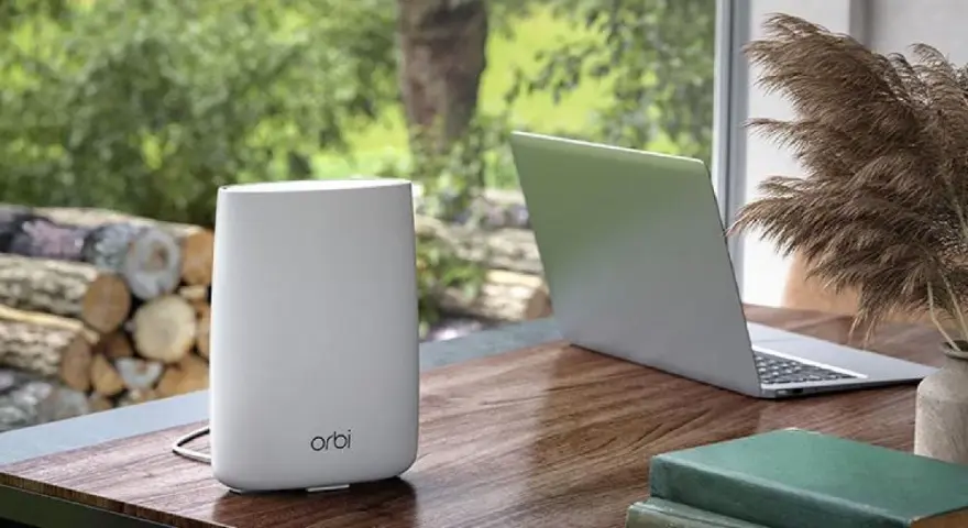Ein weißer Orbi WLAN-Router steht neben einem Laptop auf einem Holztisch.