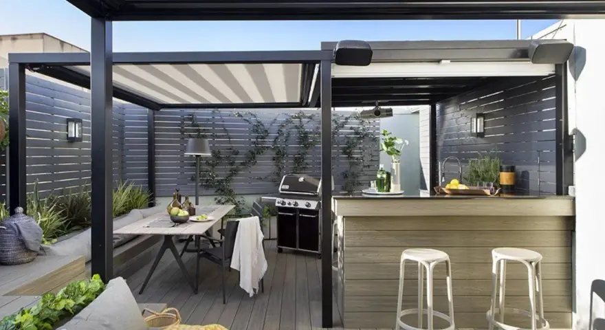Porche moderno con mesa, parrilla y una barra de bar, ideal para disfrutar de una cocina exterior.