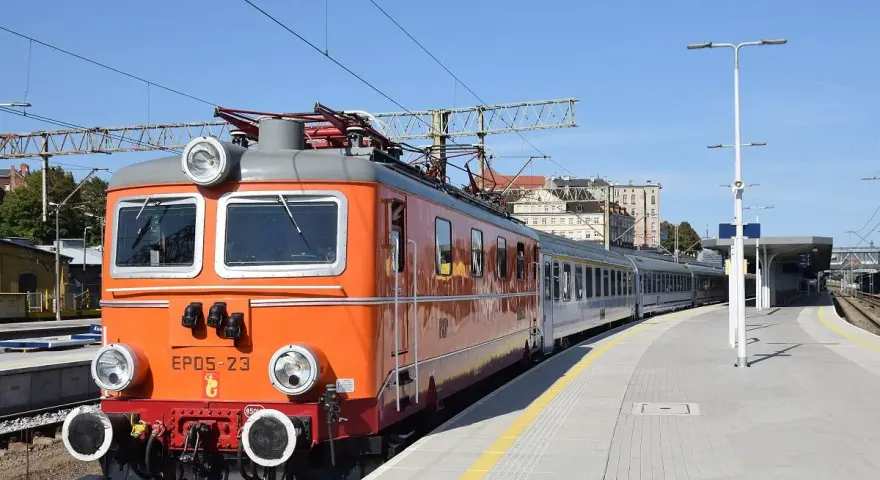 Pomarańczowa lokomotywa EP05-23, znana jako "eic chrobry", stoi na stacji. Pociąg jest gotowy do podróży.