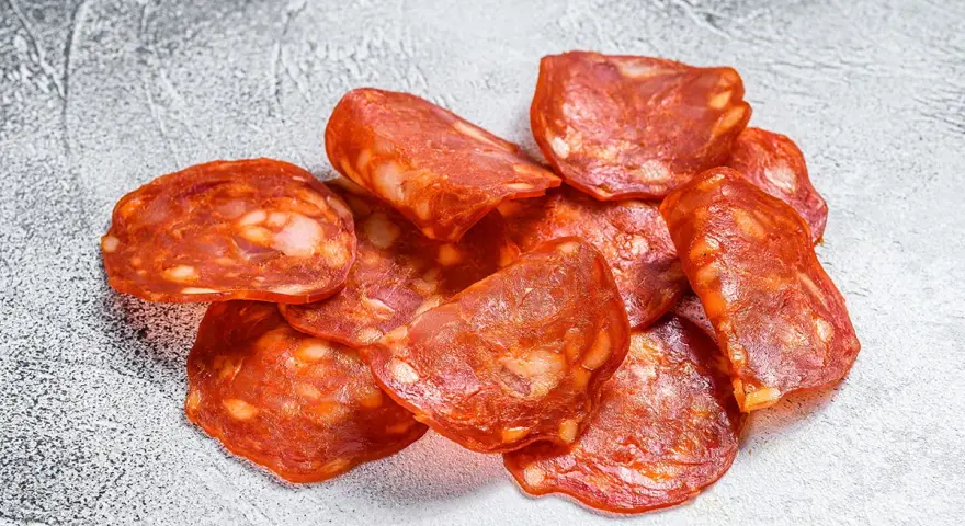 Plasterki pikantnego chorizo, wędzonej kiełbasy wieprzowej, z widocznymi kawałkami tłuszczu.