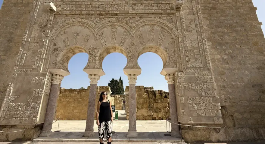 Mujer posa ante arcos de Medina Azahara. Se puede visitar Medina Azahara por libre, explorando su rica historia y arquitectura.