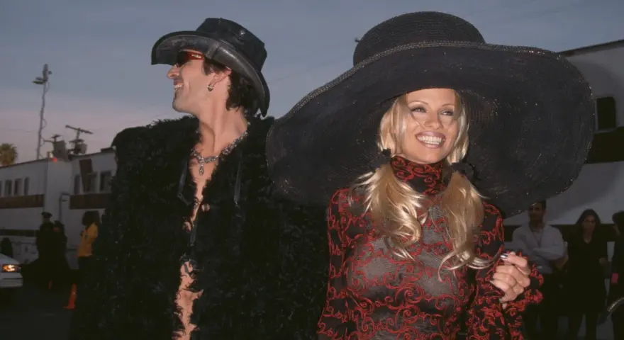 Pamela Anderson i Tommy Lee w stylizacjach z epoki. Ona w wielkim kapeluszu i wzorzystej sukience, on w kowbojskim kapeluszu i futrzanej kurtce.