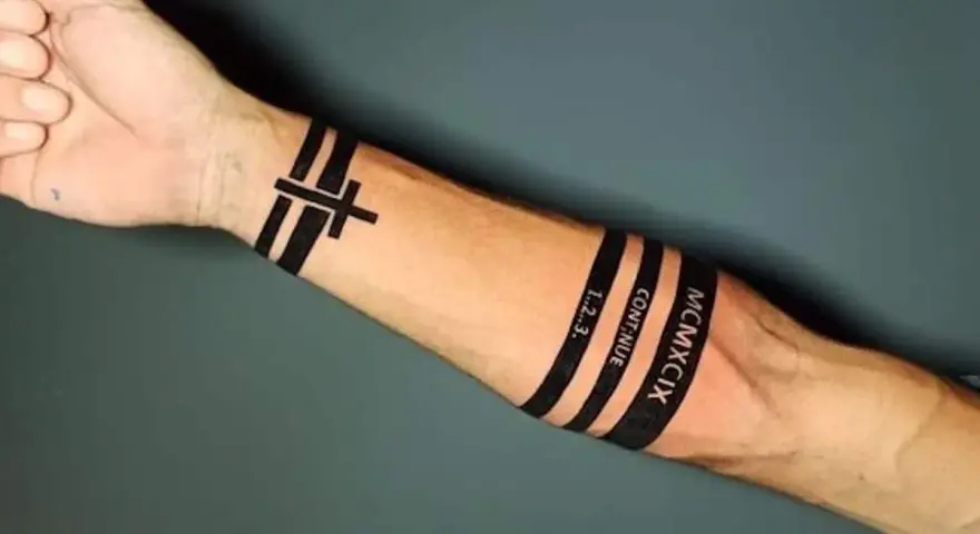 Czarny tatuaż pasek na przedramieniu z krzyżem, napisem "CONTINUE", "1..2..3." i rzymską liczbą MCMXCIX.