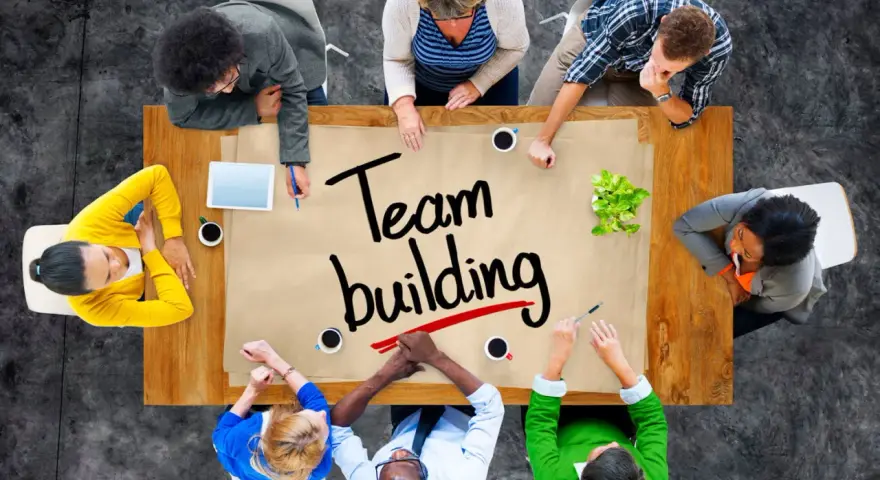 Un groupe diversifié autour d'une table discute de "team building". Ils collaborent, partageant des idées pour renforcer leur unité.