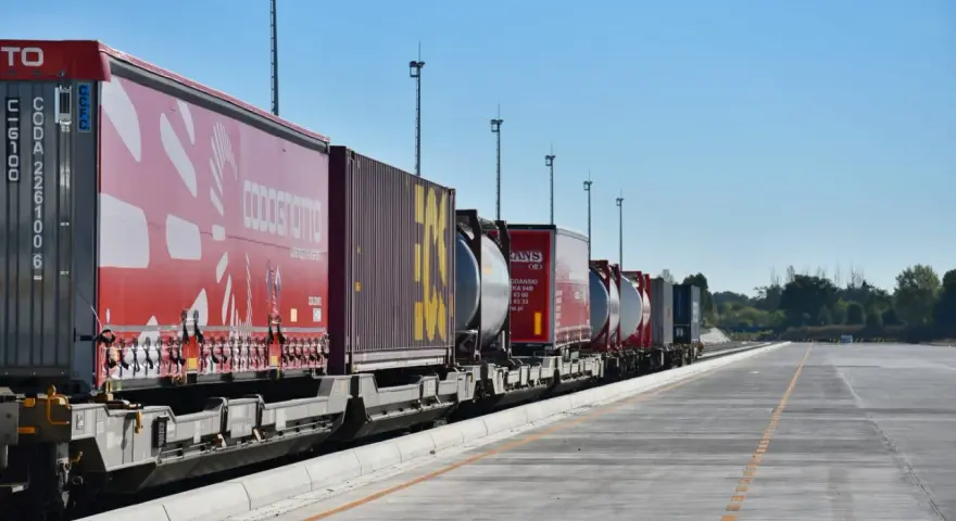 Długi pociąg towarowy z kontenerami, w tym czerwonymi z logo COSCO i żółtymi, czeka na dalszy transport kolejowy.