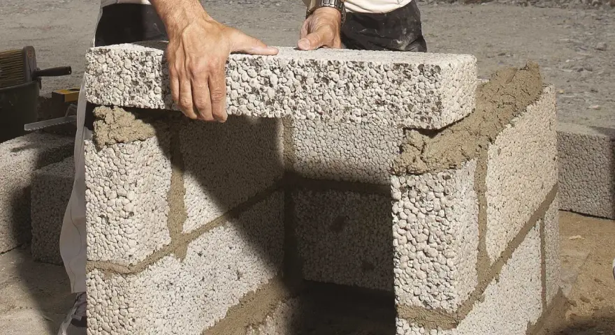 Byggare lägger mura lecablock på betongplatta. Murbruket syns mellan blocken.
