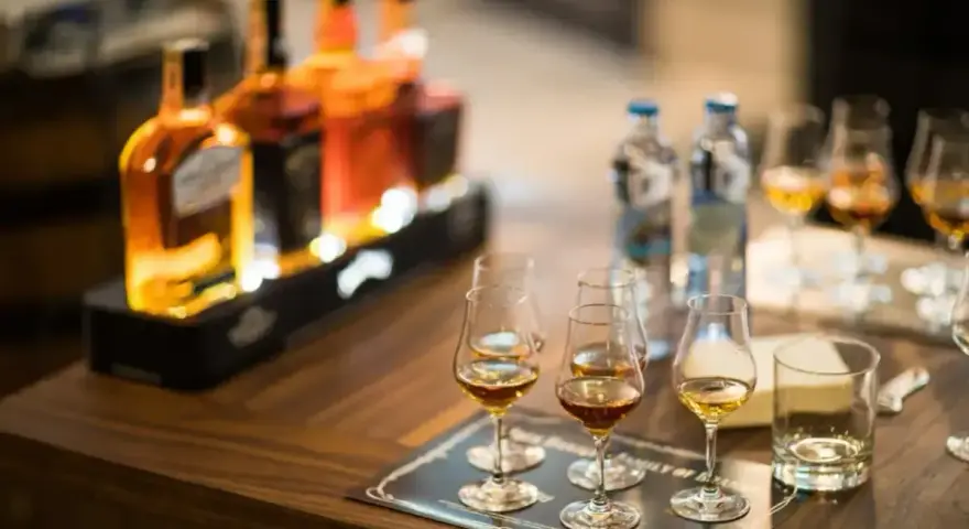 Degustacja whisky, czy to bimber? Butelki i kieliszki z bursztynowym trunkiem na drewnianym stole.
