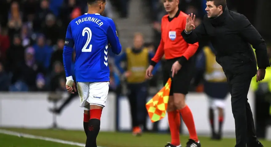 Piłkarz Rangers, Tavernier, słucha trenera. Sędzia liniowy z chorągiewką stoi obok.