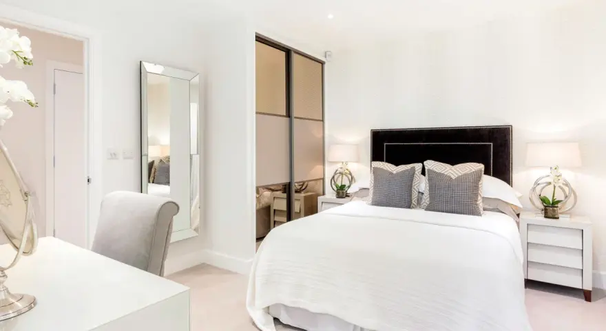 Elegante camera da letto senza finestra, con letto bianco, specchio a figura intera e un angolo toeletta.