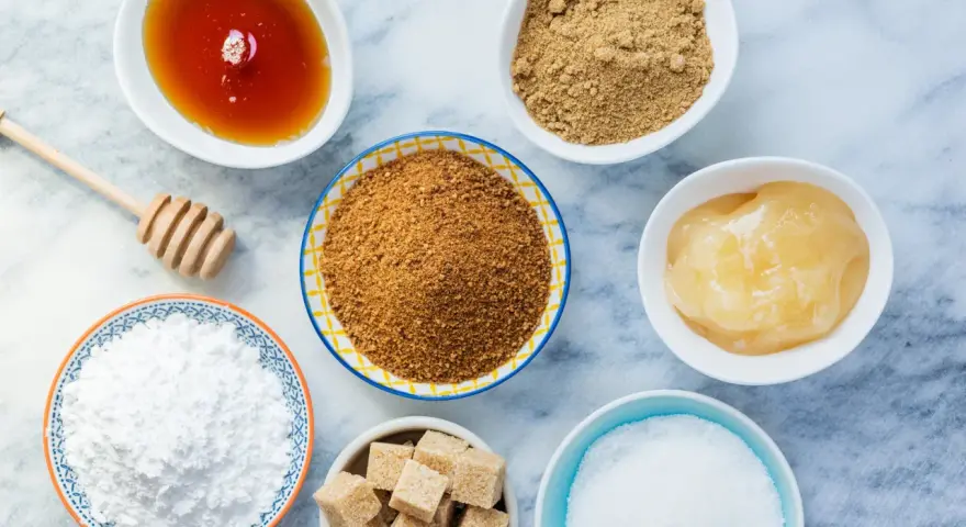 Verschiedene Süßungsmittel: Honig, brauner Zucker, Puderzucker und Würfelzucker. Hier finden Sie Alternativen, wenn Sie braunen Zucker ersetzen möchten.