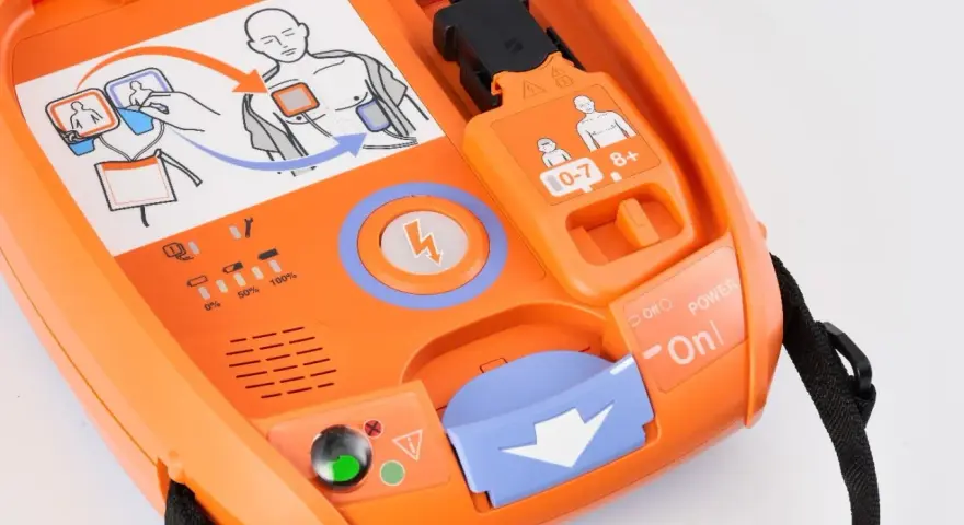 Pomarańczowy defibrylator AED z instrukcją użycia i wskaźnikami.