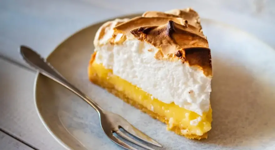 Rebanada de lemon pie con merengue dorado y relleno cremoso, lista para ser disfrutada con un tenedor.