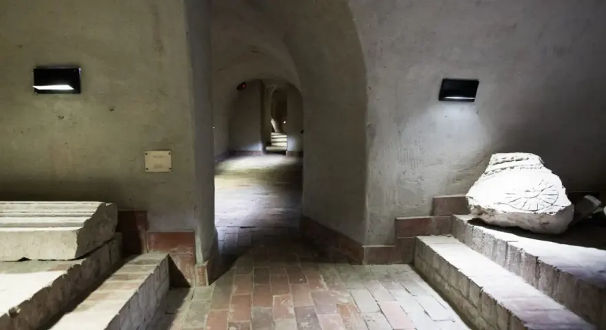 Kamienne korytarze i łuki tworzą tajemniczą trasę podziemną w Lublinie. Widać fragmenty dawnych budowli i artefakty.