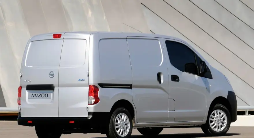 Srebrny Nissan NV200, wszechstronny van, zaparkowany przed nowoczesnym budynkiem.