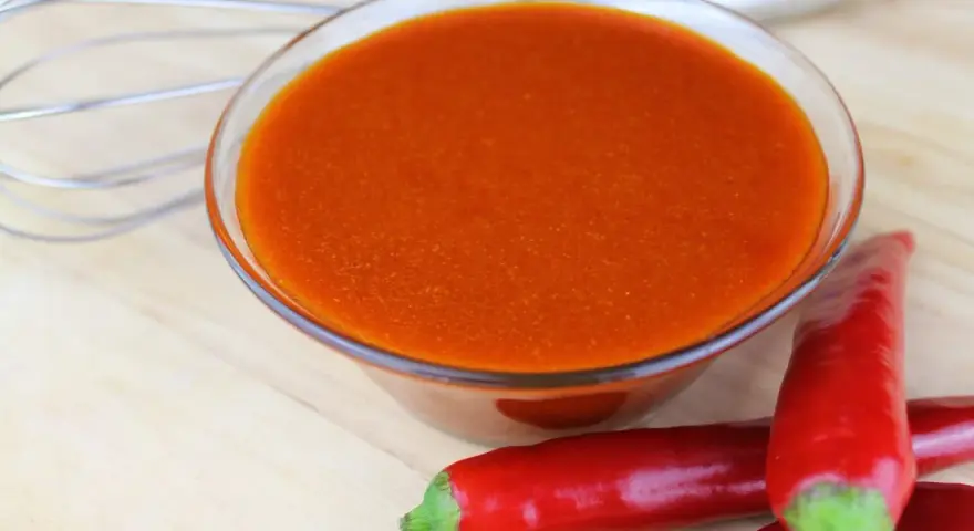 Schüssel mit leuchtend orangeroter Buffalo Sauce, daneben rote Chilis und ein Schneebesen. Perfekt für Flügel!