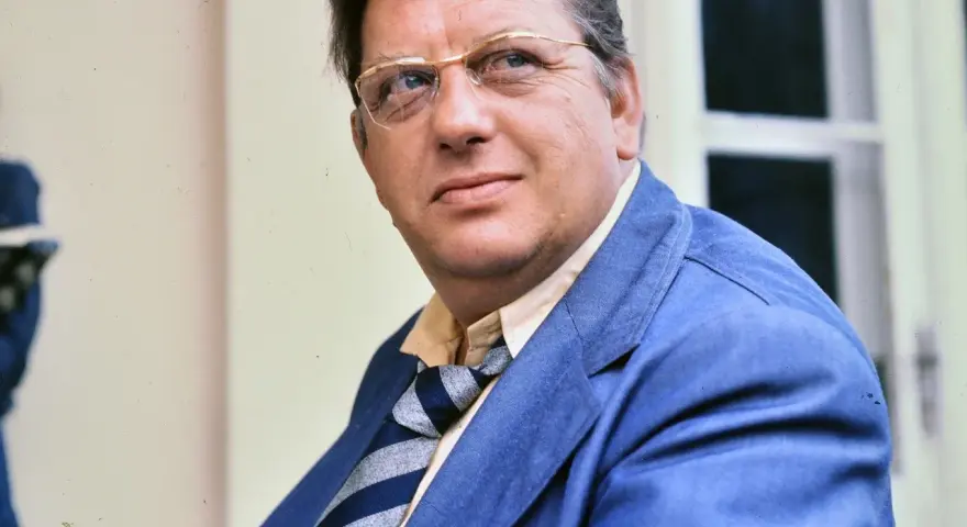 Portret Mariusza Dmochowskiego w okularach i niebieskiej marynarce. W tle okno.