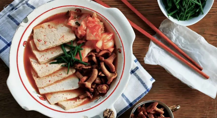 Pyszne kimchi jjigae z tofu i grzybami, podane z zieloną cebulką.