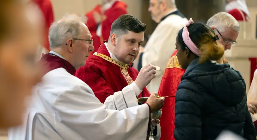 Clergy in red robes perform communion, a sacred act that can be seen as a form of evangelizing, sharing faith with a young woman.