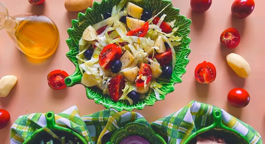 Un'insalata di patate napoletana colorata con pomodorini, olive e lattuga, servita in una ciotola a forma di foglia.