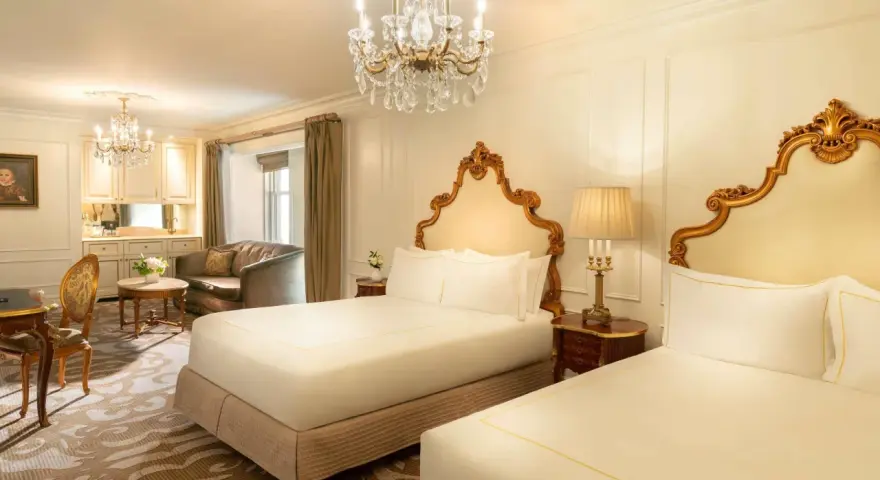 Luksusowy pokój z dwoma łóżkami w hotelu Plaza w Nowym Jorku, z kryształowym żyrandolem i złotymi zdobieniami. Zastanawiasz się, ile kosztuje noc w hotelu Plaza w Nowym Jorku?