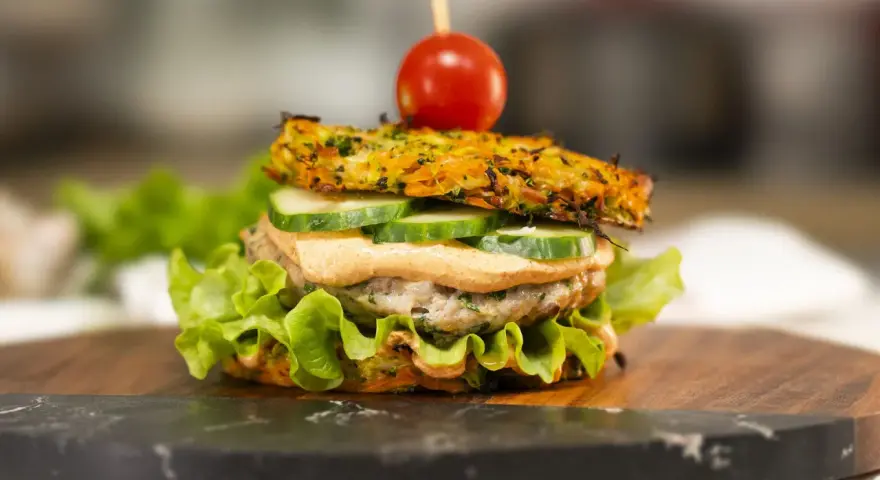 Burger z warzywną bułką, kotletem, ogórkiem, sosem i pomidorkiem na wykałaczce.