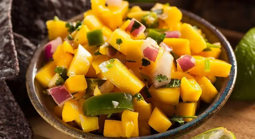 En skål med färgglad mango salsa, med tärnad mango, rödlök, grön paprika och koriander. Serveras med tortillachips och limeklyftor.