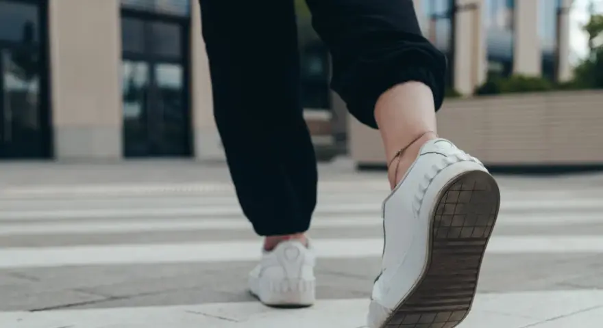 Kobieta w białych sneakersach idzie po pasach, licząc ile kroków dziennie.
