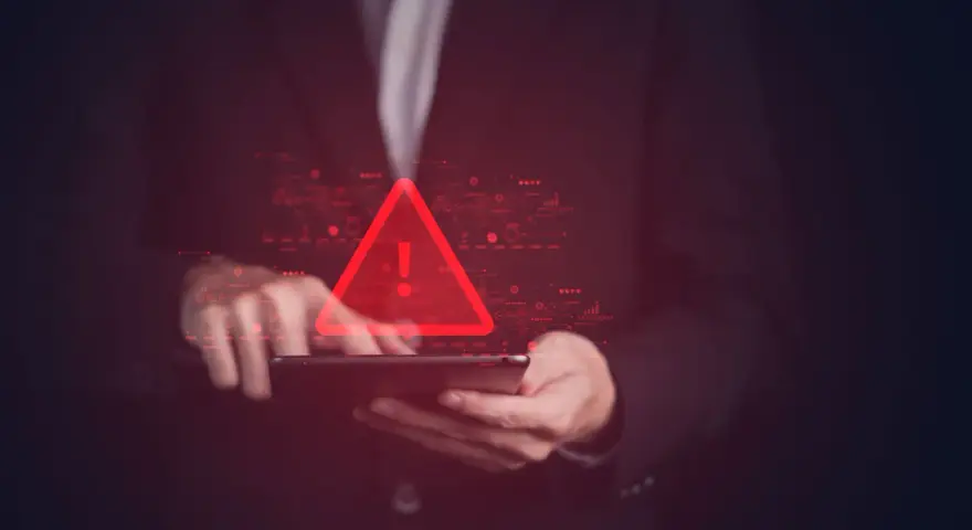 Czerwony trójkąt z wykrzyknikiem nad tabletem, symbolizujący groźbę karalną w cyfrowym świecie.