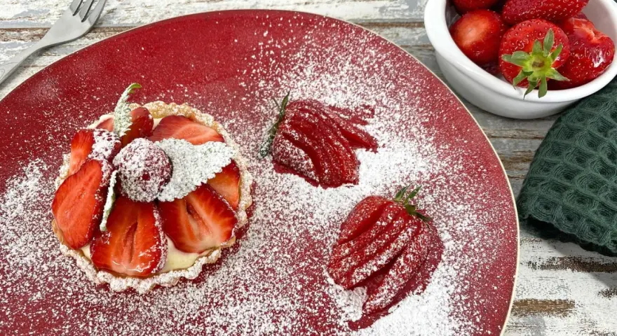 Zuckersüße Erdbeer Tartelettes, bestäubt mit Puderzucker, auf rotem Teller. Daneben frische Erdbeeren und eine Gabel.