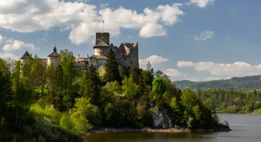 Zamek w Czorsztynie góruje nad jeziorem, otoczony zielenią. W oddali widać góry.