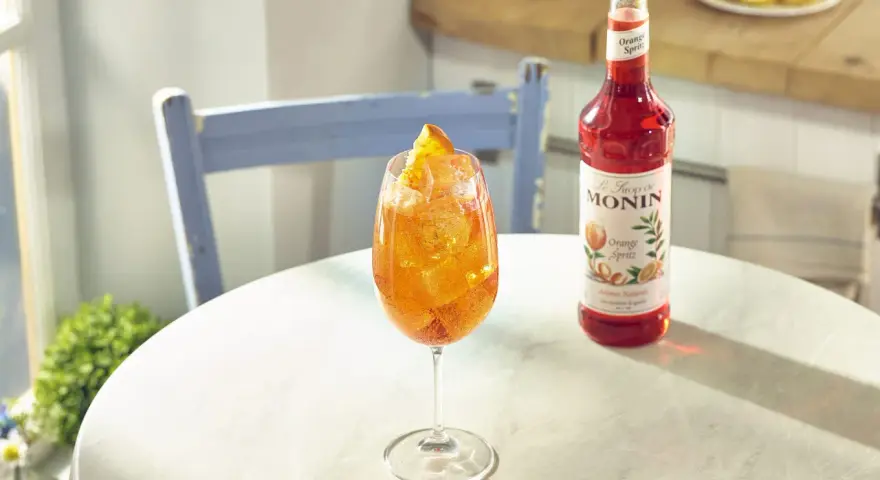 Orzeźwiający drink z syropem Monin Orange Spritz, lodem i pomarańczą. Idealny przepis na letnie popołudnie.