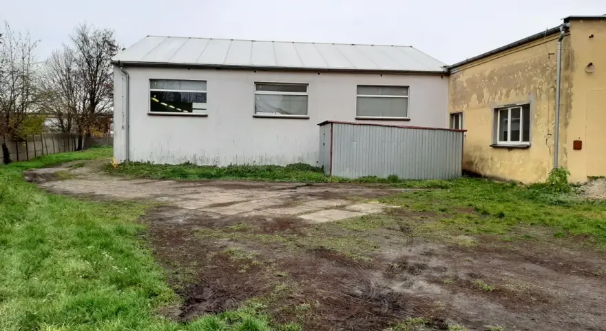 Teren wokół budynków jest nierówny, z błotnistymi śladami i trawą. Widać tu różne formy terenu, od płaskich placów po lekko nachylone trawniki.