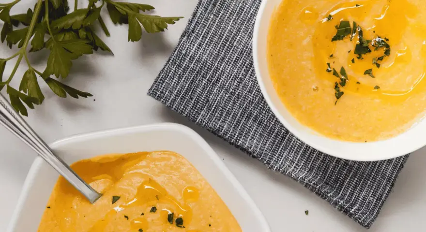 Deux bols de velouté de butternut facile, ornés d'huile d'olive et de persil frais, prêts à être dégustés.