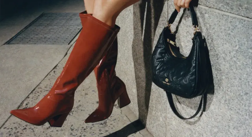 Kobieta w czerwonych kozakach i pikowanej torebce z logo Nine West. Nine West to znana marka obuwia i akcesoriów.