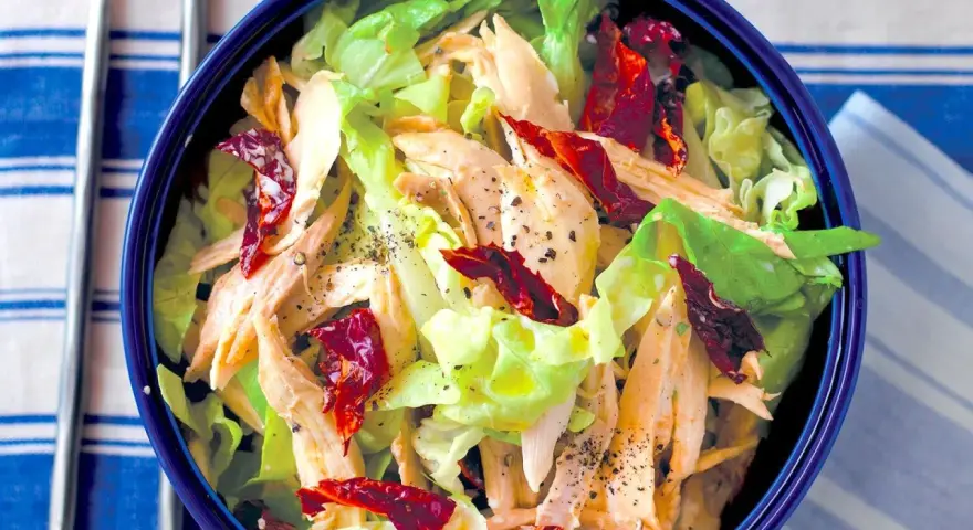 Insalata di pollo lesso con lattuga croccante e pomodori secchi, condita con pepe nero macinato.