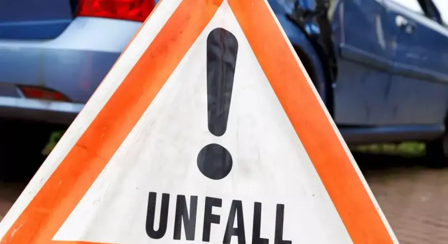 Warnschild "Unfall" vor beschädigtem Auto. Nach einem Verkehrsunfall kann eine Vorstandsbeschwerde bei der Versicherung nötig sein.