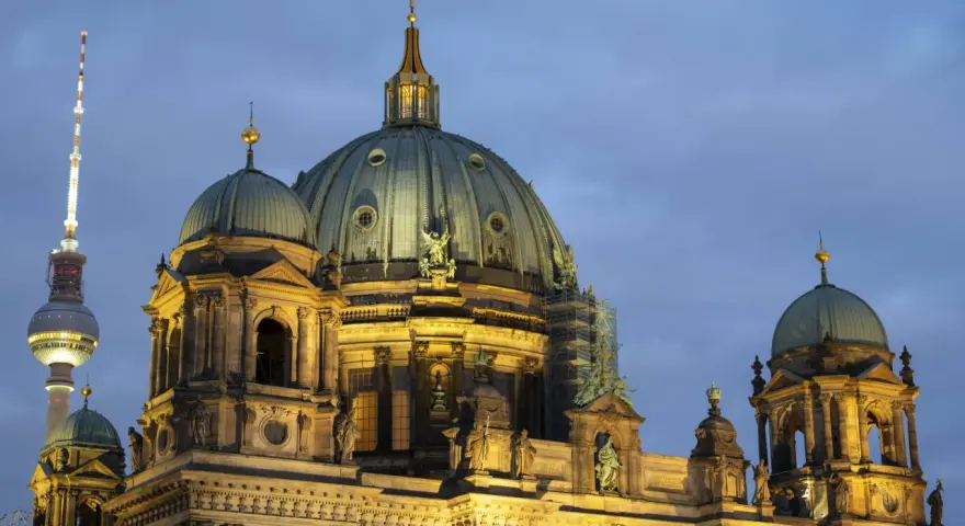 Prachtvolle Kuppeln des Berliner Doms im Abendlicht, mit dem Fernsehturm im Hintergrund. Ein Wahrzeichen der Kirchen in Berlin.