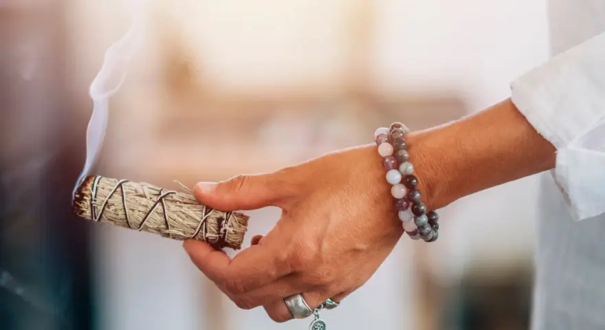 Mano con un manojo de salvia humeante, lista para sahumar la casa y purificar el ambiente.