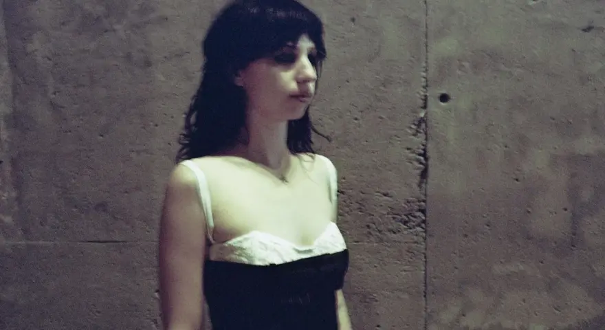 Stella Rose Gahan w czarnej sukience z białym gorsetem, stoi przy betonowej ścianie.