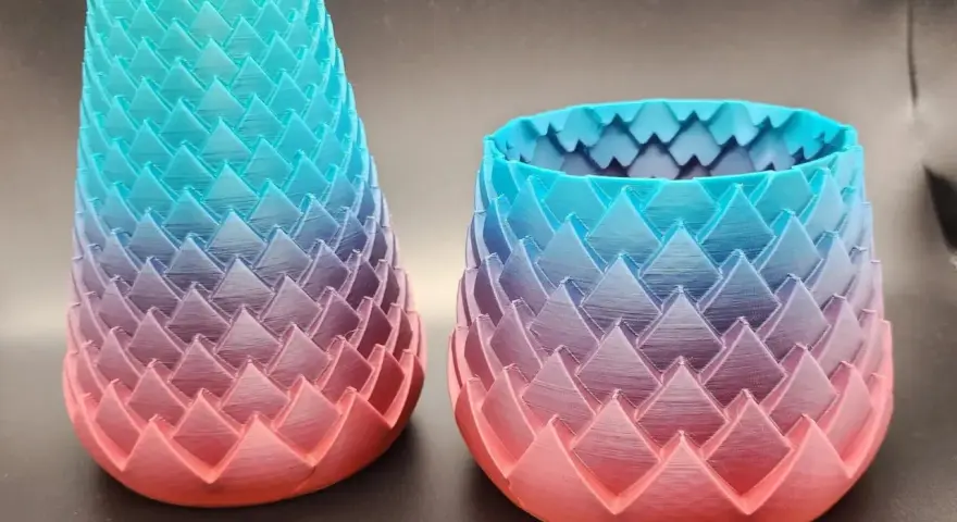 Two dragon-scale patterned vases, created with color 3d printing, showcase a gradient from coral pink to teal blue.