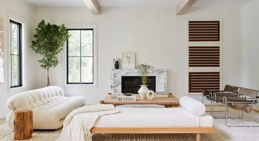 Elegante salón con decoración blanco y madera natural. Sofá curvo blanco, diván de madera, chimenea de mármol y plantas.