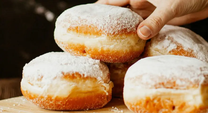 Stos puszystych pączków oprószonych cukrem pudrem. Idealne na tłusty czwartek, te fit pączki kuszą apetycznym wyglądem.
