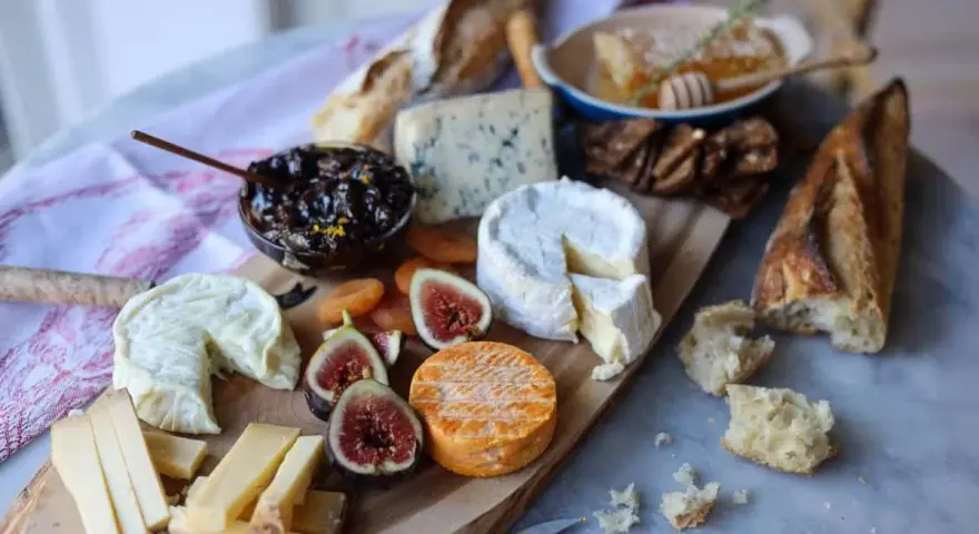 Plateau de fromages variés, dont un fromage à pâte cuite, avec figues, confiture et pain.