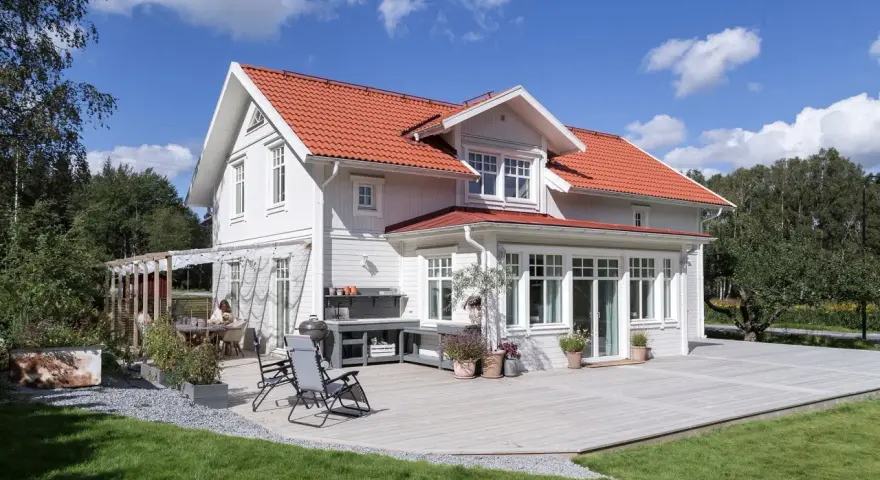 Vitt hus med rött tak och stor altan. Perfekt för att behandla altan och njuta av sommaren.