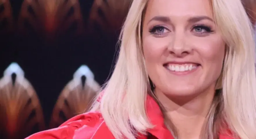 Uśmiechnięta blondynka w czerwonej marynarce, z błękitnymi oczami i delikatnym naszyjnikiem. Ola, jaka to melodia?