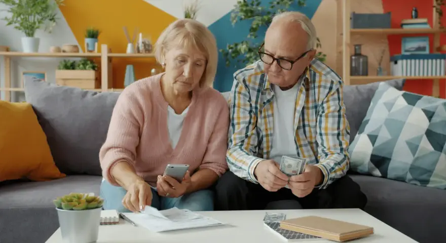 Couple âgé examinant des documents et de l'argent, peut-être pour une déclaration fiscale ou un article 83 CGI.