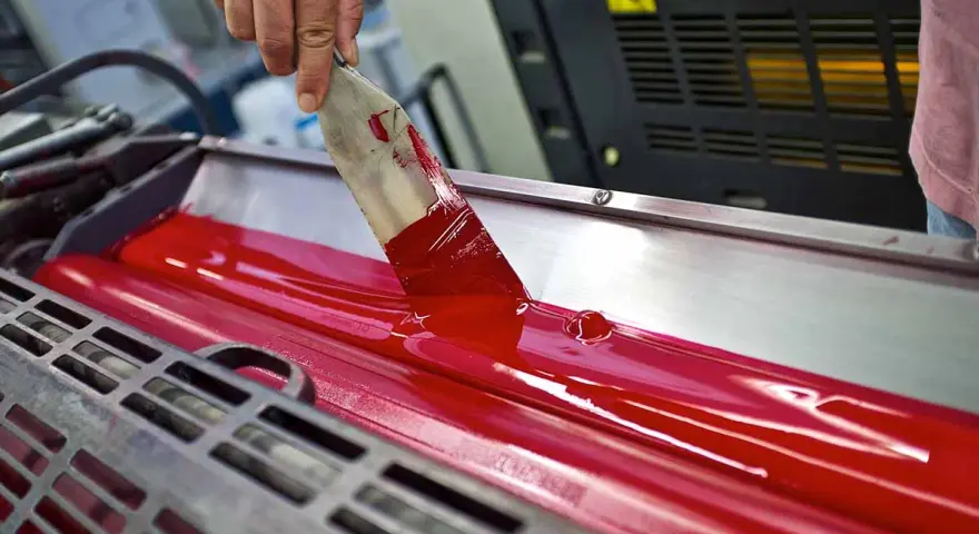 Mano esparciendo tinta roja en rodillos de imprenta, mostrando las ventajas de la imprenta para la difusión masiva de información.